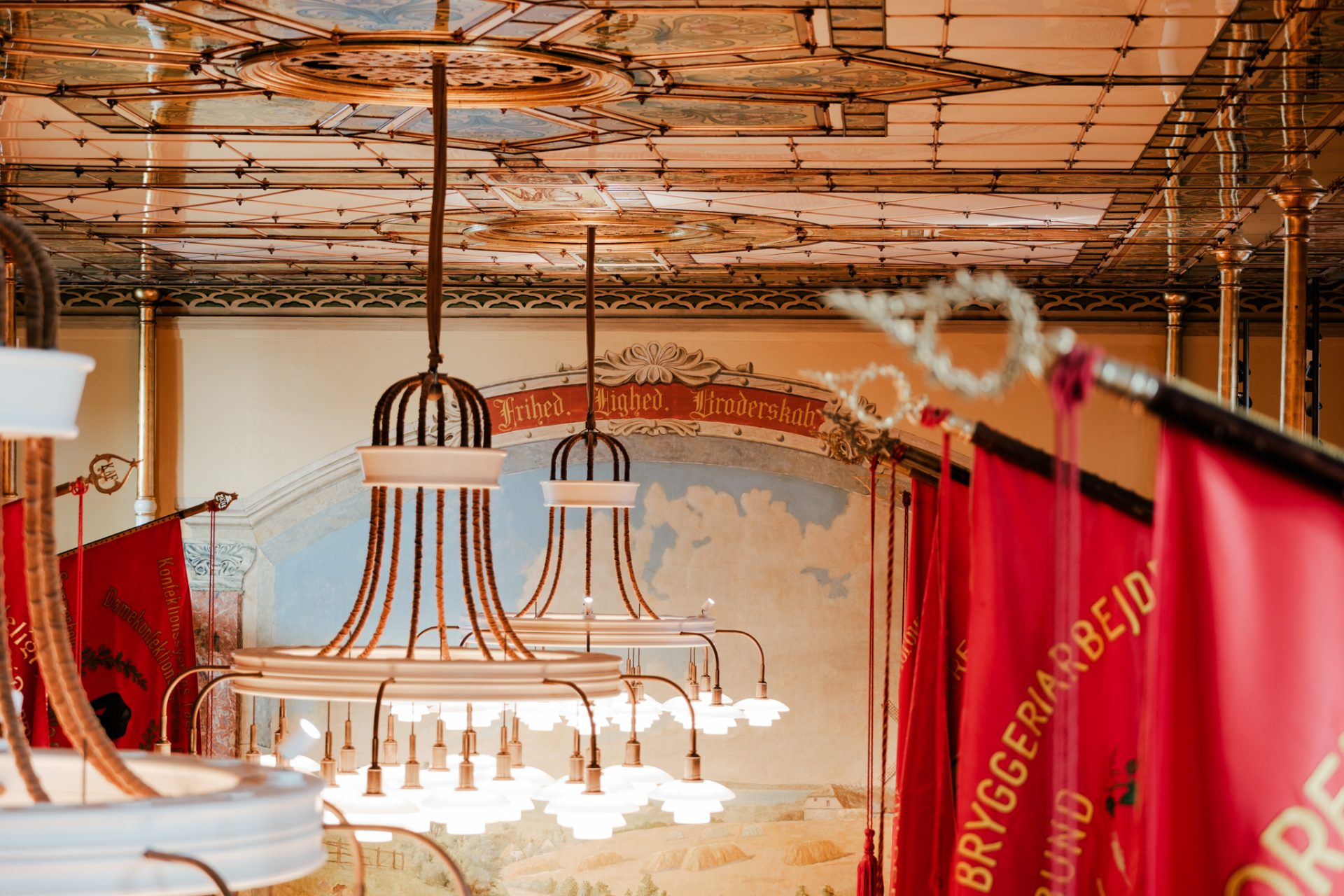 Udsigt fra balkonen i festsalen mod billedet på bagvæggen med faner, lamper foran.