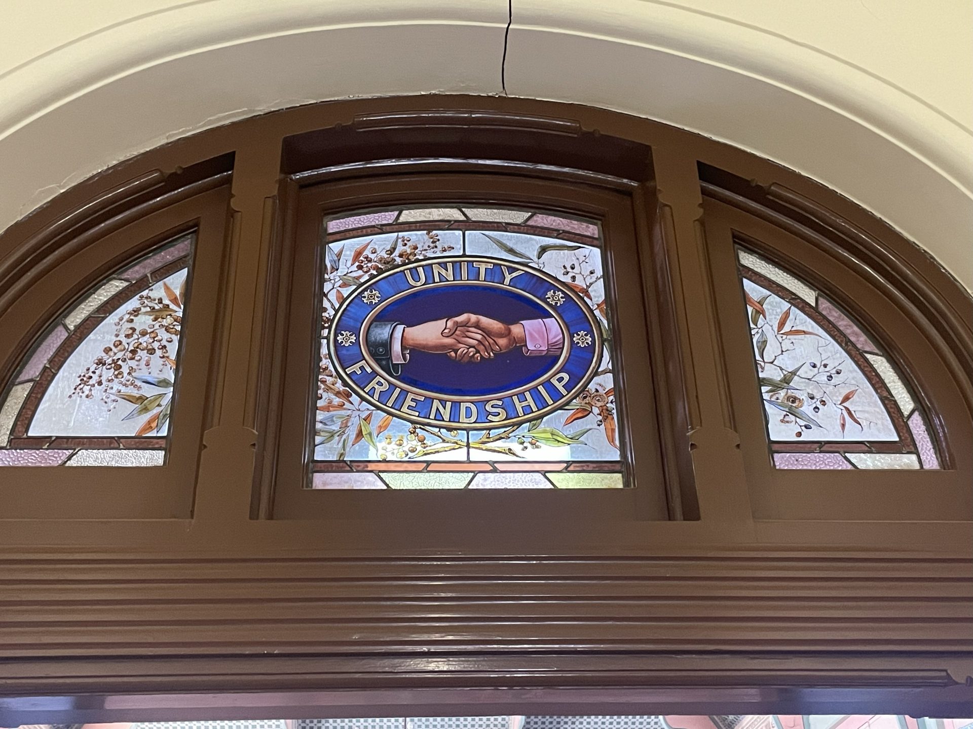 Glasmaleri i vindue over en dør i Broken Hill Trades Hall, viser håndtryk mellem arbejdsgiver og arbejder, over 