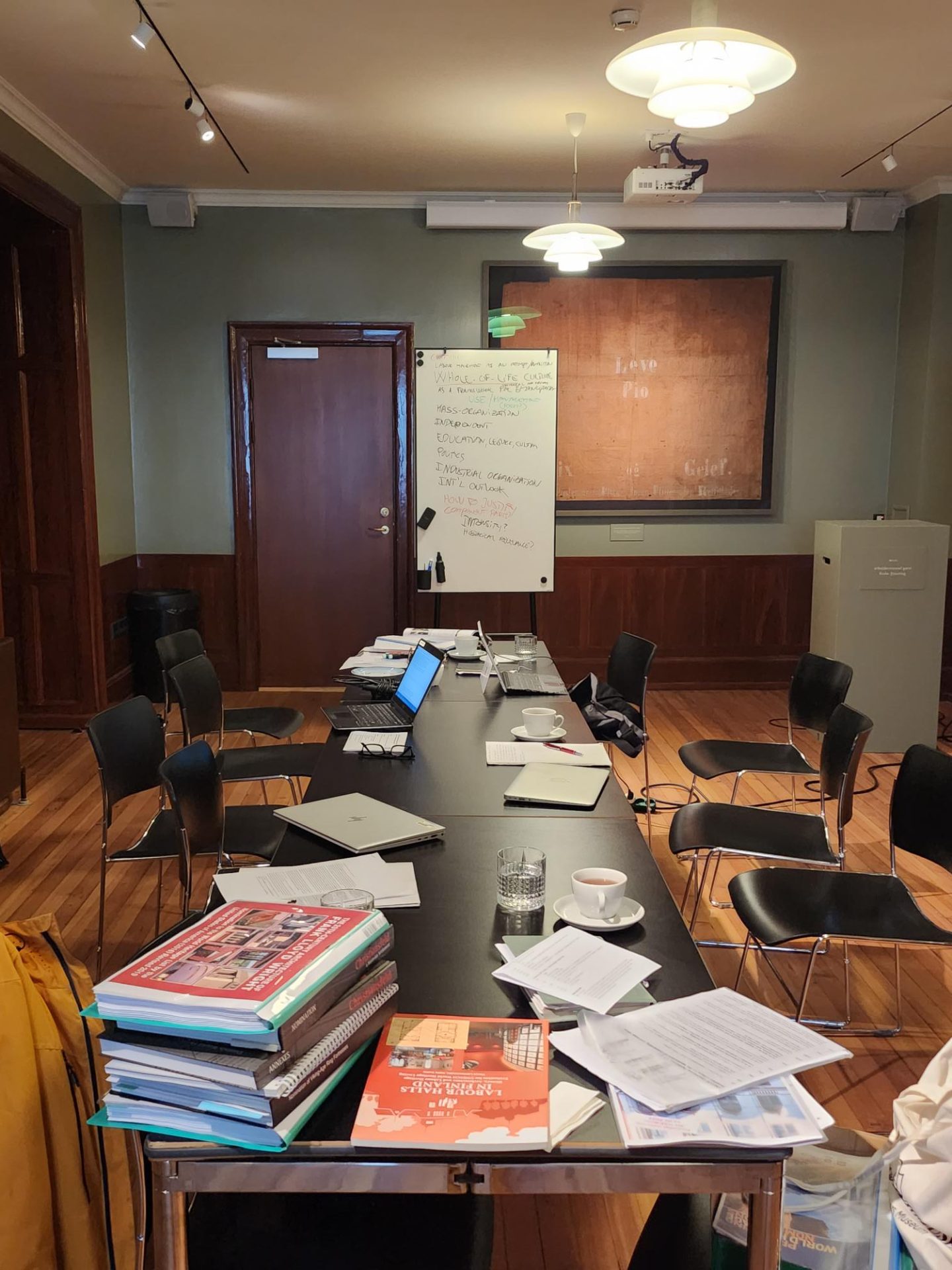 Mødelokale på Arbejdermuseet under workshop, bordet er fyldt med bøger og laptops. 